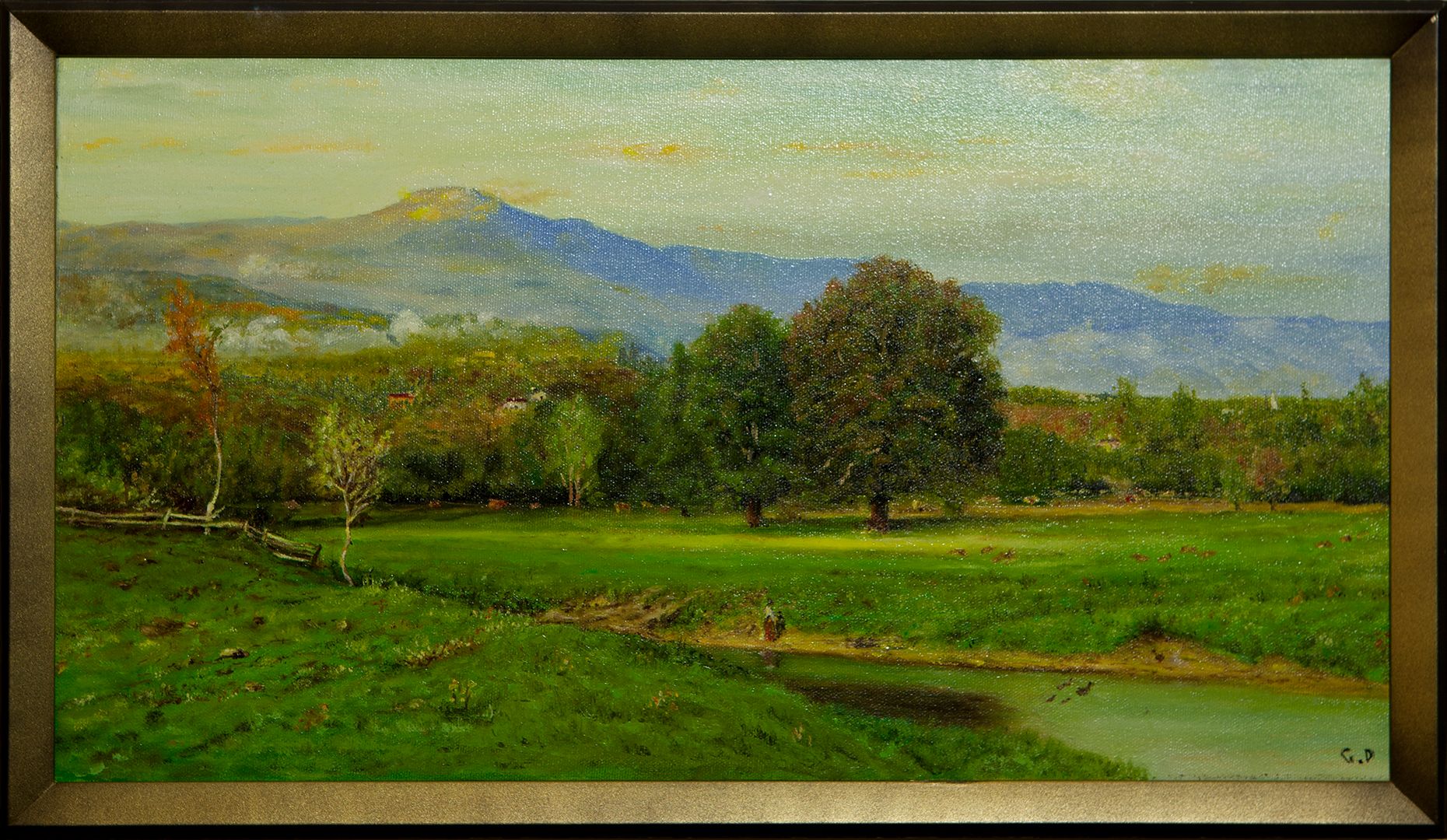 A wide, sunlit pasture with a stream and a few large trees, a wooden fence, and a hazy blue mountain on the horizon.
